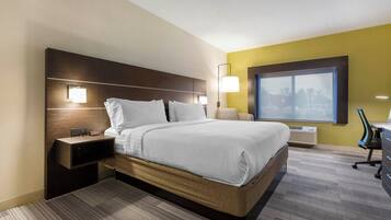 Habitación de hotel con cama, mesita de noche, lámpara y ventana con vista a la ciudad.