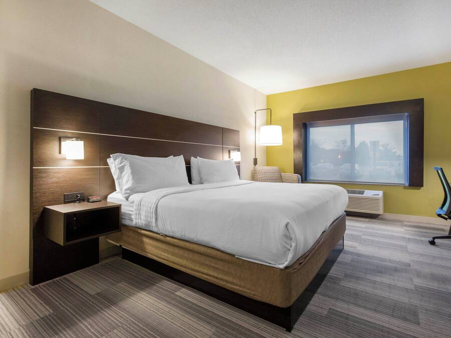 Habitación de hotel con cama, mesita de noche, lámpara y ventana con vista a la ciudad.