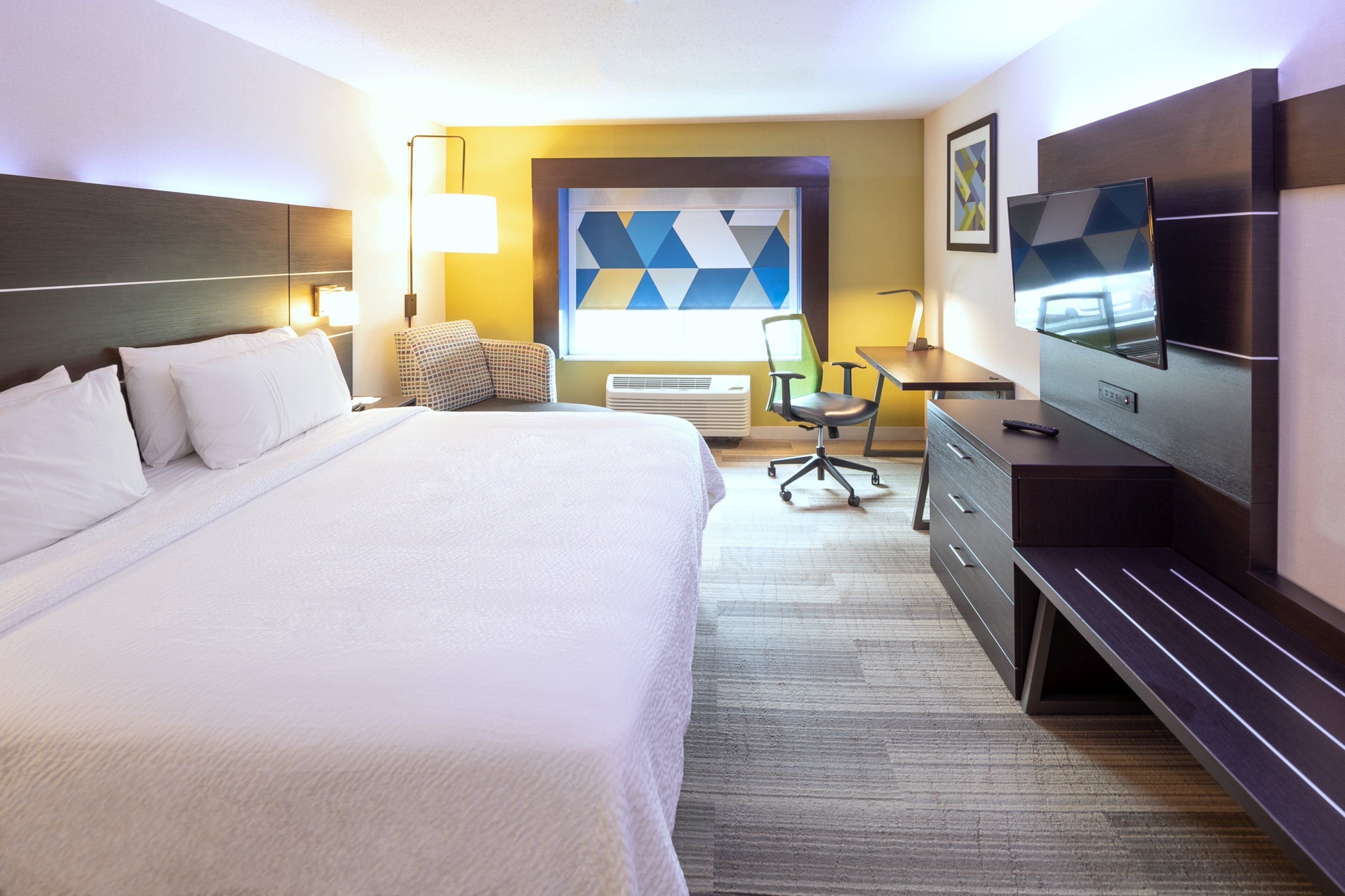 Habitación de hotel con una cama grande, un escritorio con silla, un televisor de pantalla plana y una ventana con vistas geométricas.