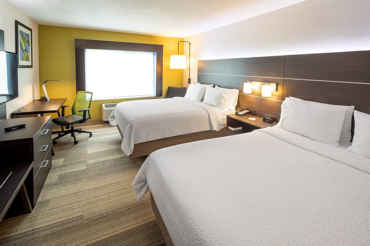 A hotel room with two beds, a desk, a chair, a lamp, and a window.