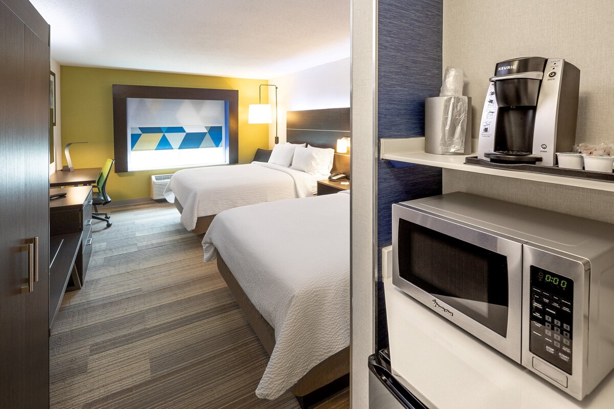 A hotel room with two beds, a microwave, a coffee maker, and a desk with a chair.