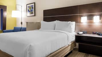 Habitación de hotel con una cama grande, un escritorio con teléfono y reloj, una lámpara y un cuadro en la pared.