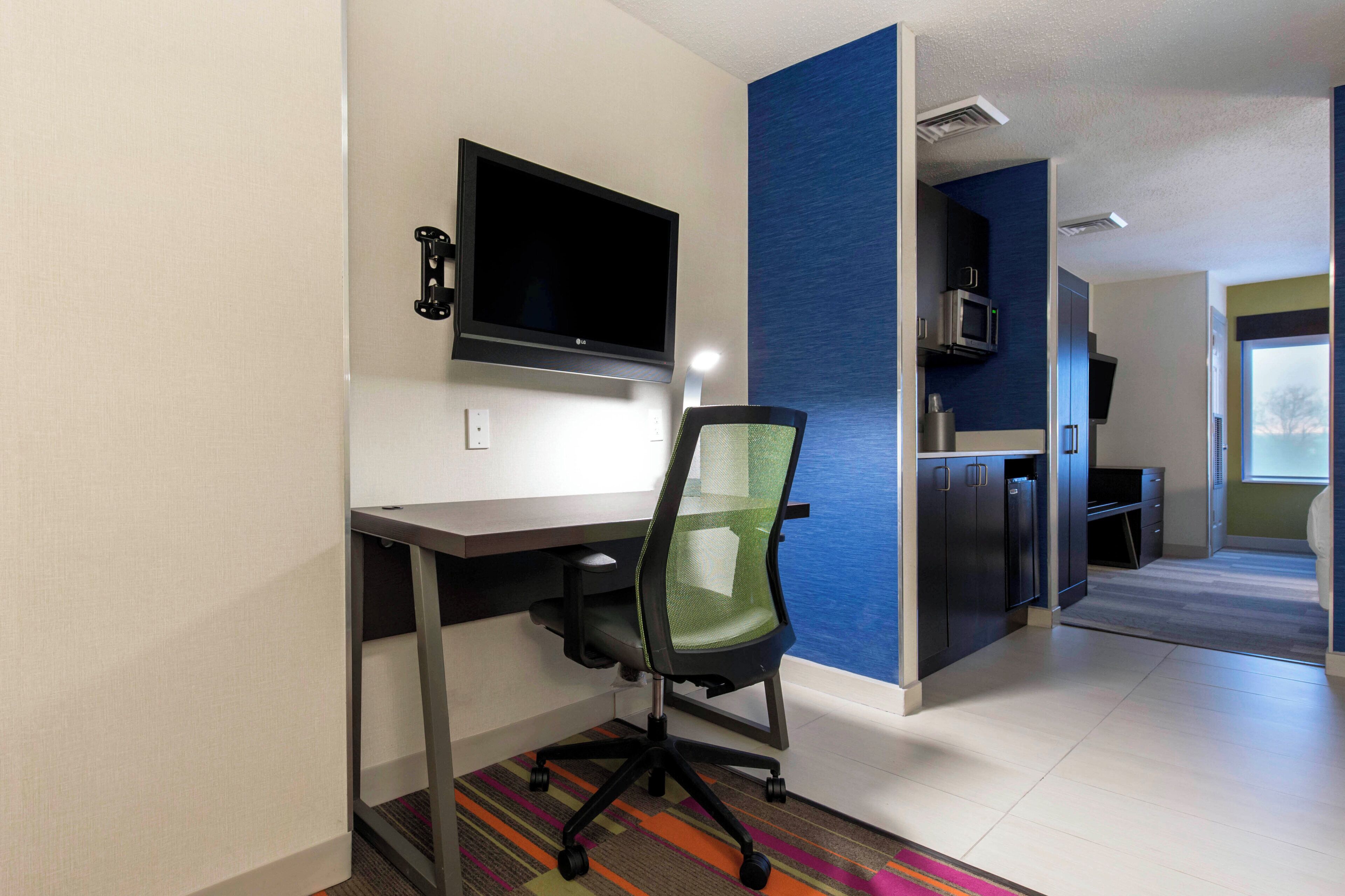 A modern office space with a flat-screen monitor, office chair, and a kitchenette area.