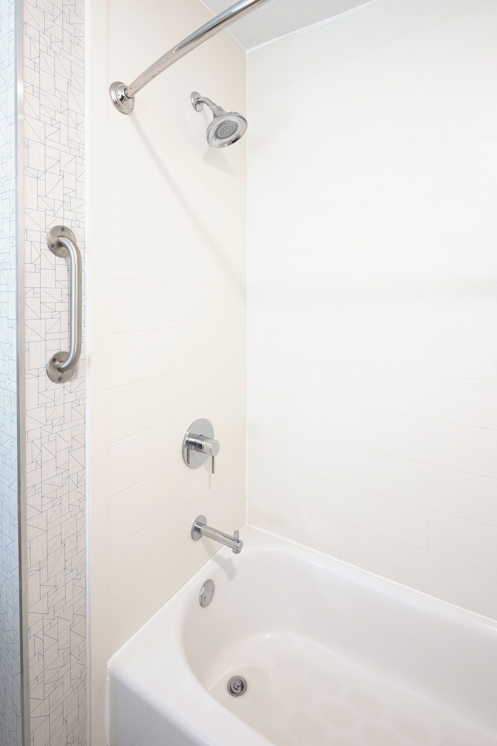 A modern bathroom with a white bathtub, a handheld showerhead, and a grab bar.