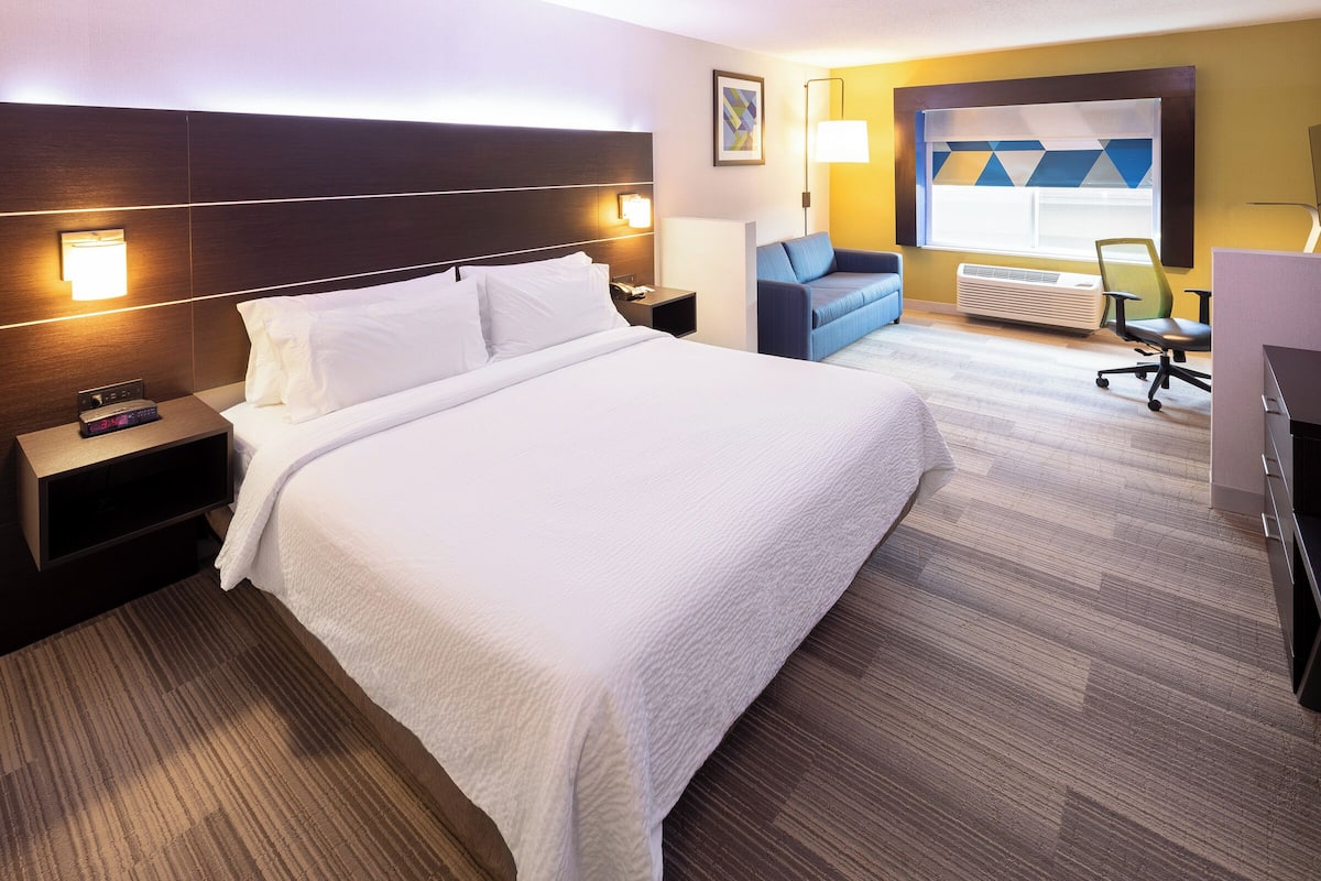 A hotel room with a large bed, a nightstand, a desk, a chair, and a window with a view.