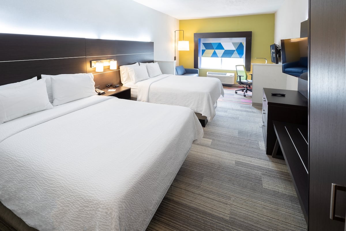 A hotel room with two beds, a desk, a chair, a TV, and a large window with a geometric wall art piece.