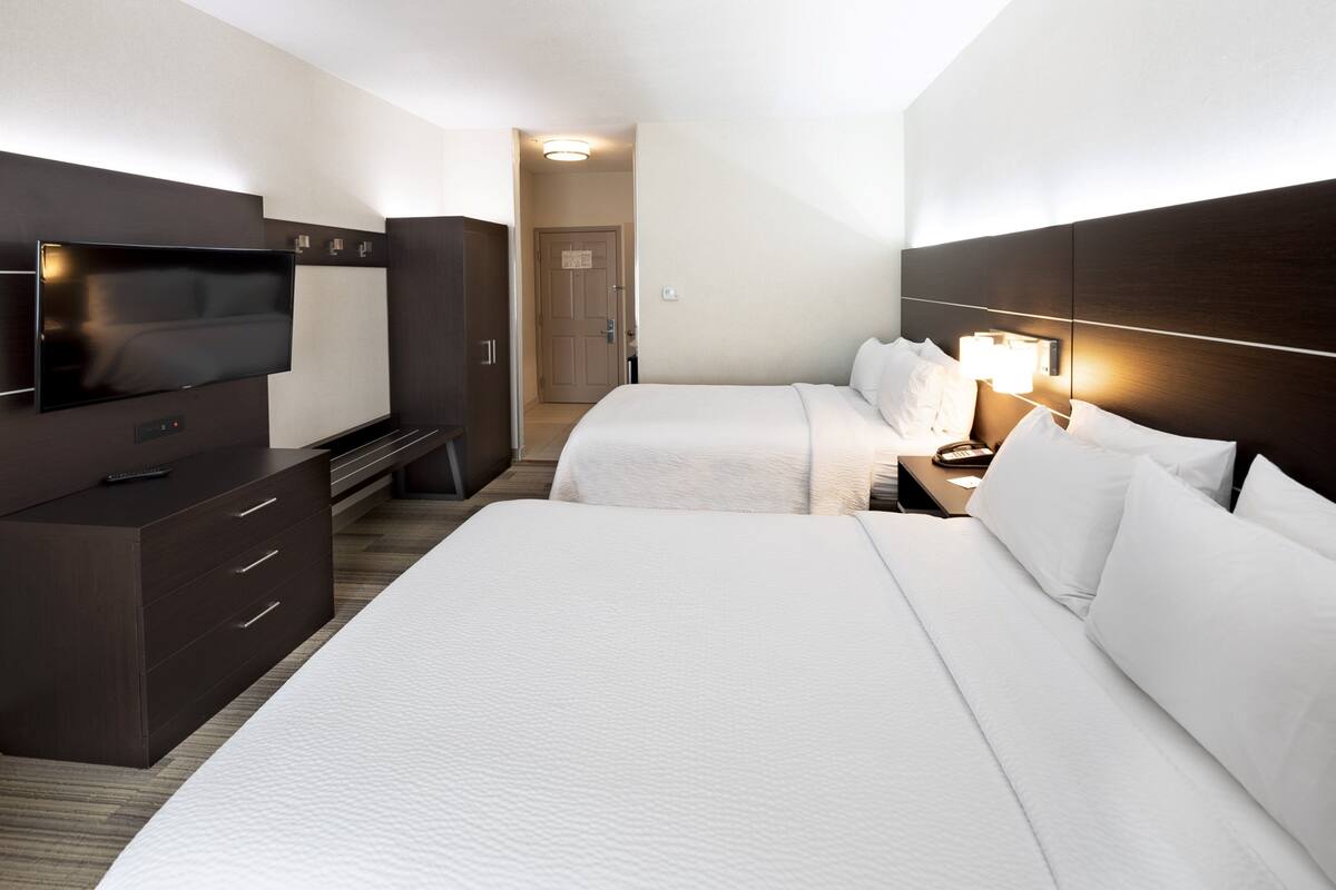 A hotel room with a large bed, a TV, a desk with drawers, and a bedside table with a lamp.
