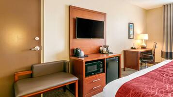 Une chambre d’hôtel comprenant un lit, un bureau avec un micro-ondes, une télévision, une chaise et une petite table avec une lampe.