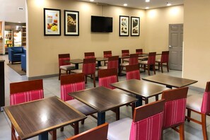 Un comedor con varias mesas y sillas, un televisor montado en la pared y cuadros enmarcados.