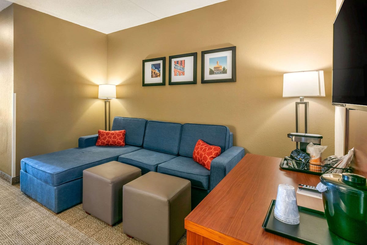 Habitación de hotel con sofá seccional, dos otomanas, una mesa de madera y tres cuadros en la pared.