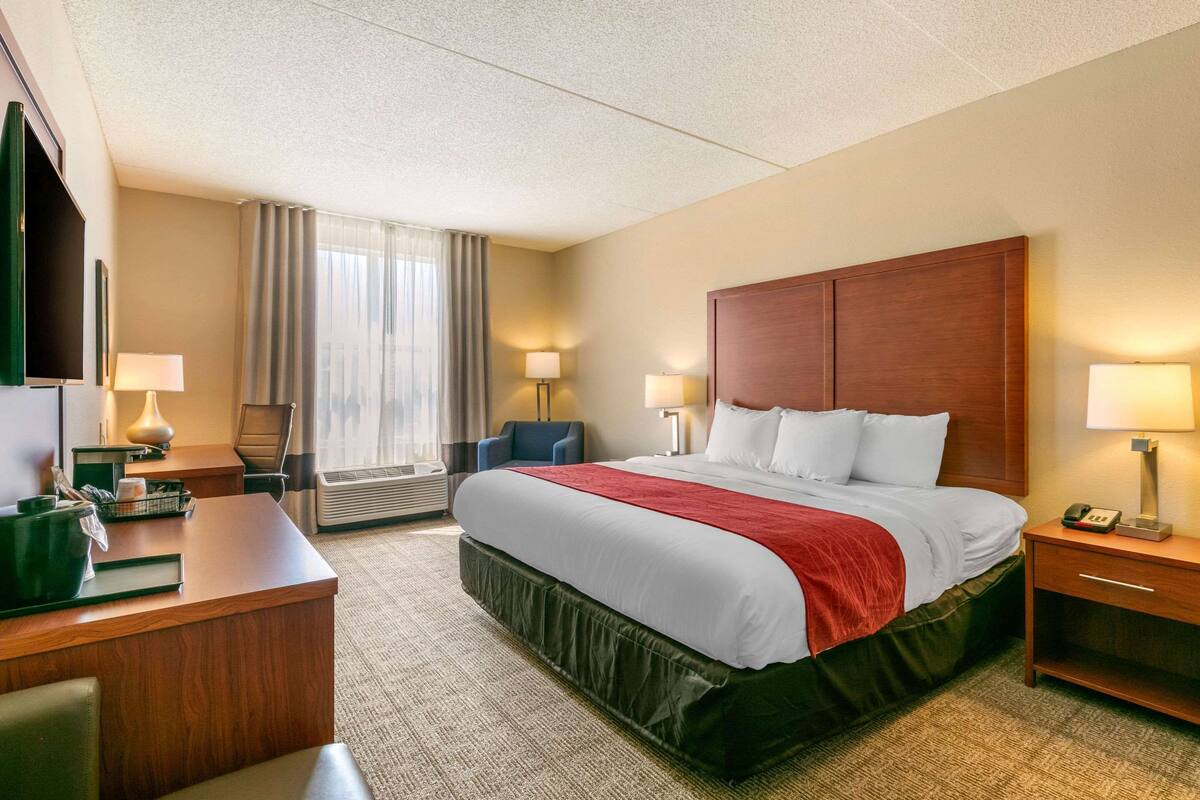 Habitación de hotel con una cama grande, un escritorio, una silla, un televisor y una ventana con cortinas.