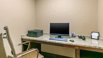 A hotel room with a desk, computer, printer, and a chair.