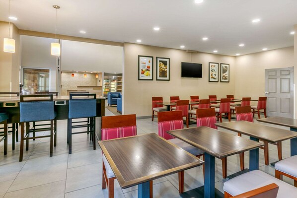 Un restaurante con varias mesas y sillas, una zona de cocina y cuadros en la pared.