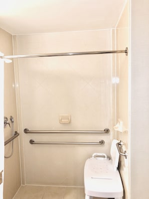 Un baño con ducha, barras de apoyo, inodoro y secador de manos.