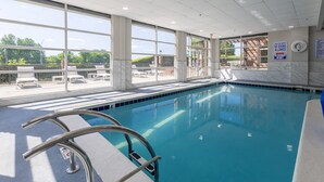 An indoor swimming pool with clear glass walls, a tiled floor, and a metal pool ladder.
