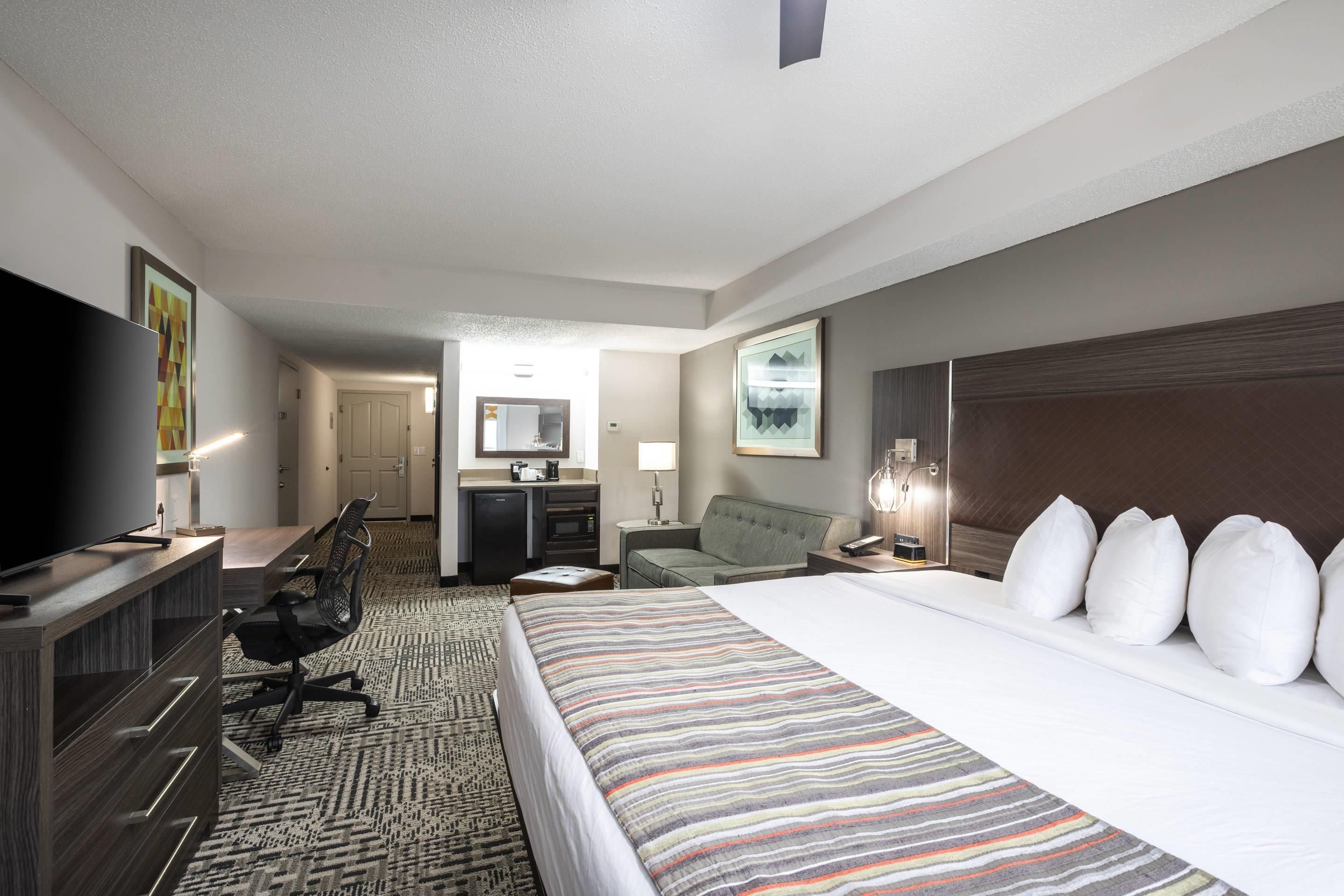 A hotel room with a large bed, a desk with a flat-screen TV, a kitchenette, and a separate bathroom.