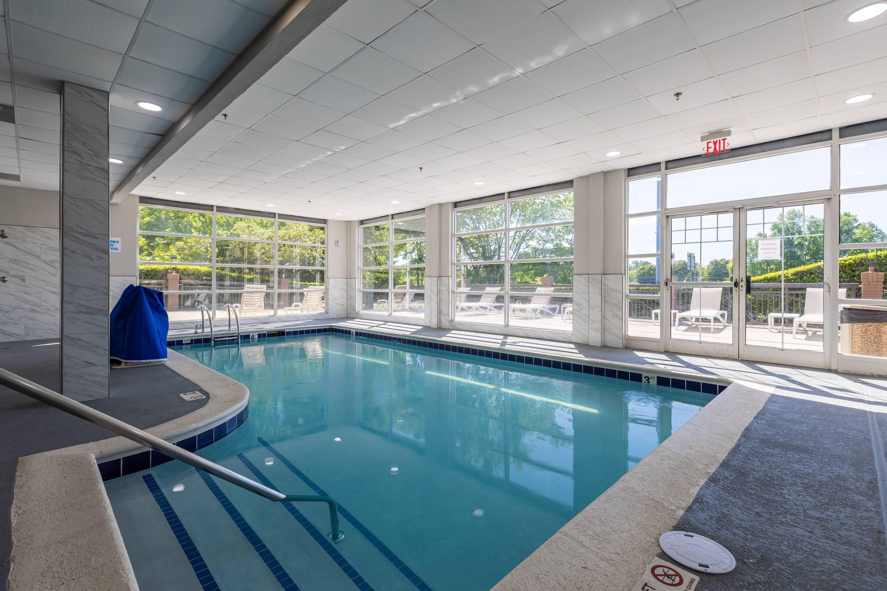An indoor swimming pool with clear glass walls, a tiled floor, and a lifeguard chair.