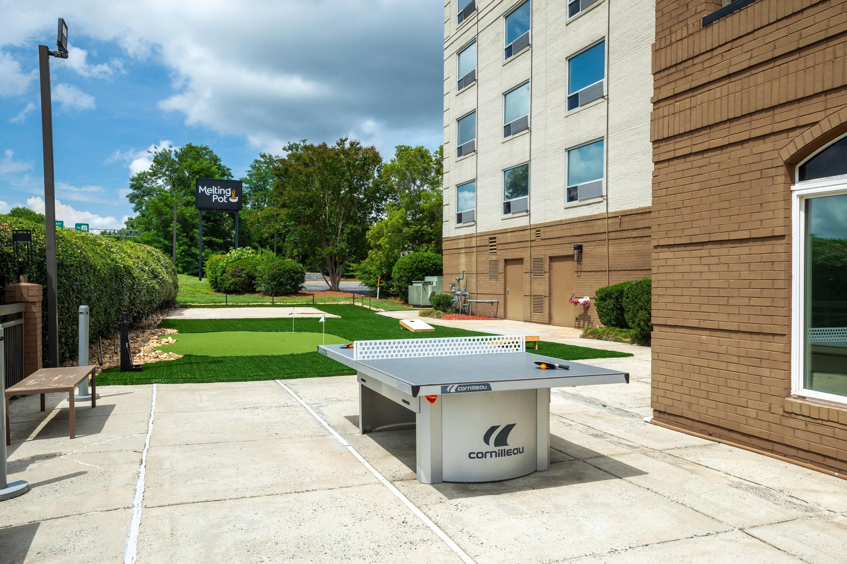 A courtyard with a foosball table, a tennis table, and a building with a sign that reads 'Melting Pot.'