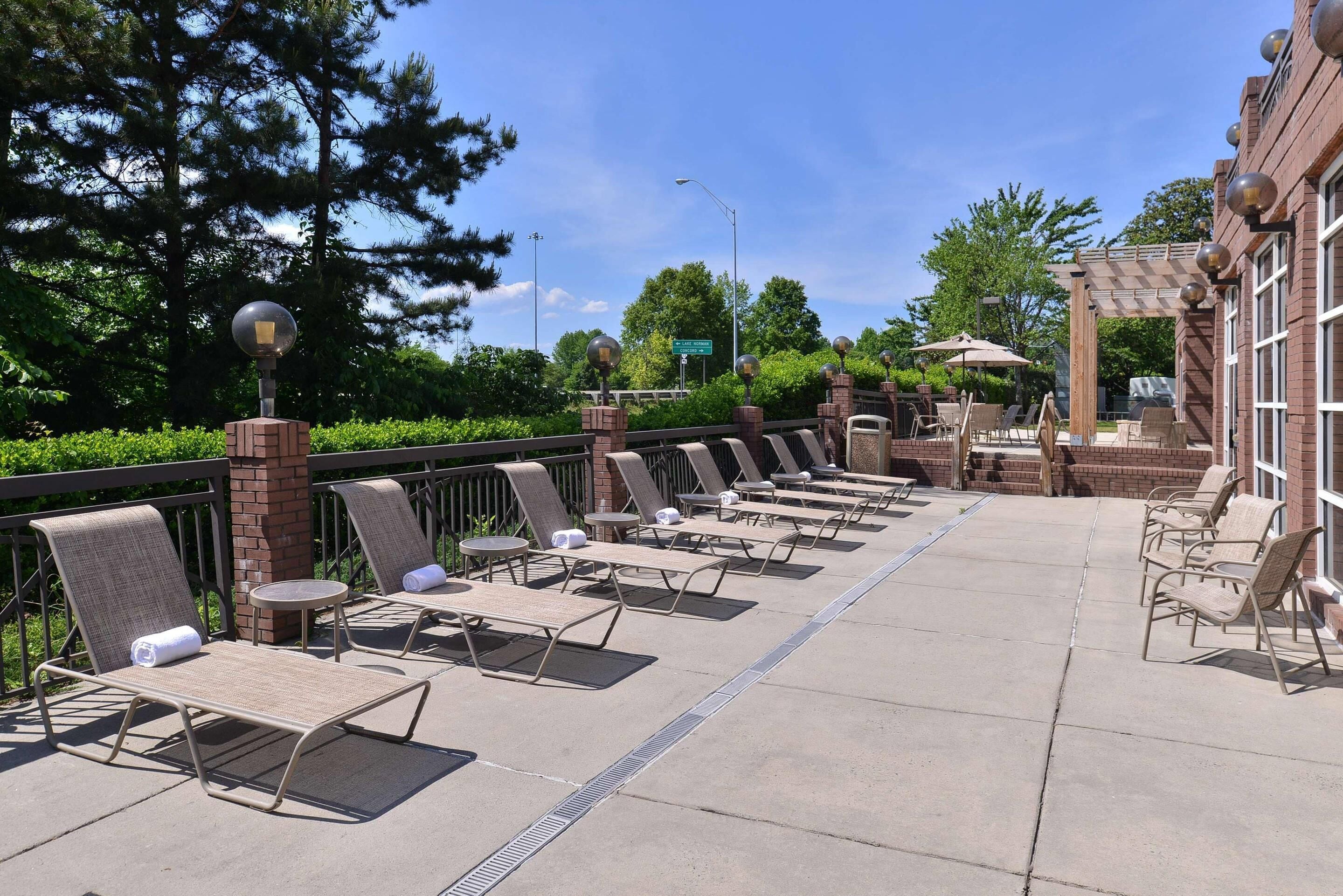 A row of sun loungers with umbrellas, a brick wall, and a pergola with outdoor seating.