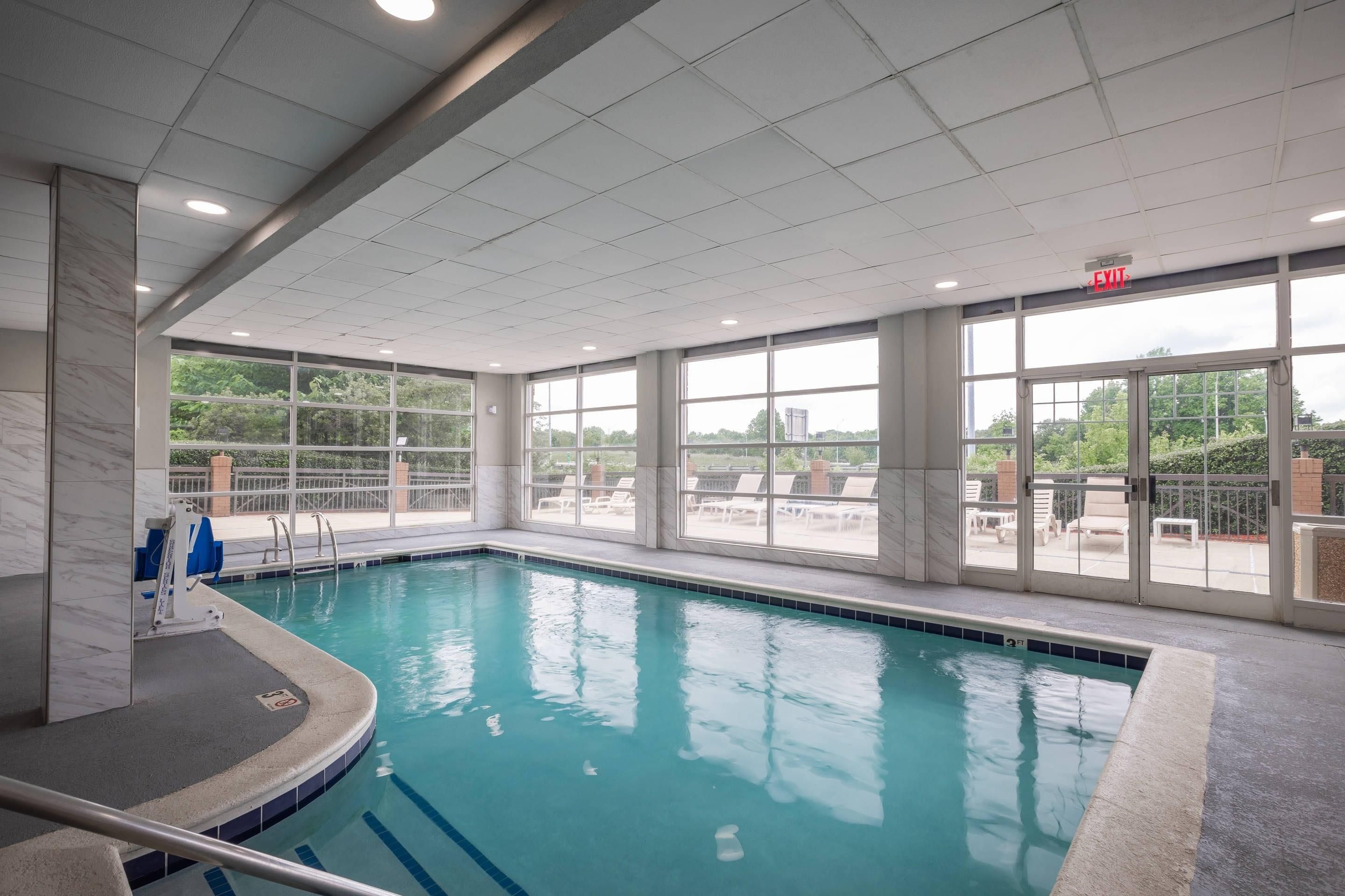 En indendørs swimmingpool med glasvægge, fliseloft og et synligt skilt til udgang.