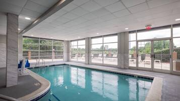 En indendørs swimmingpool med glasvægge, fliseloft og et synligt skilt til udgang.