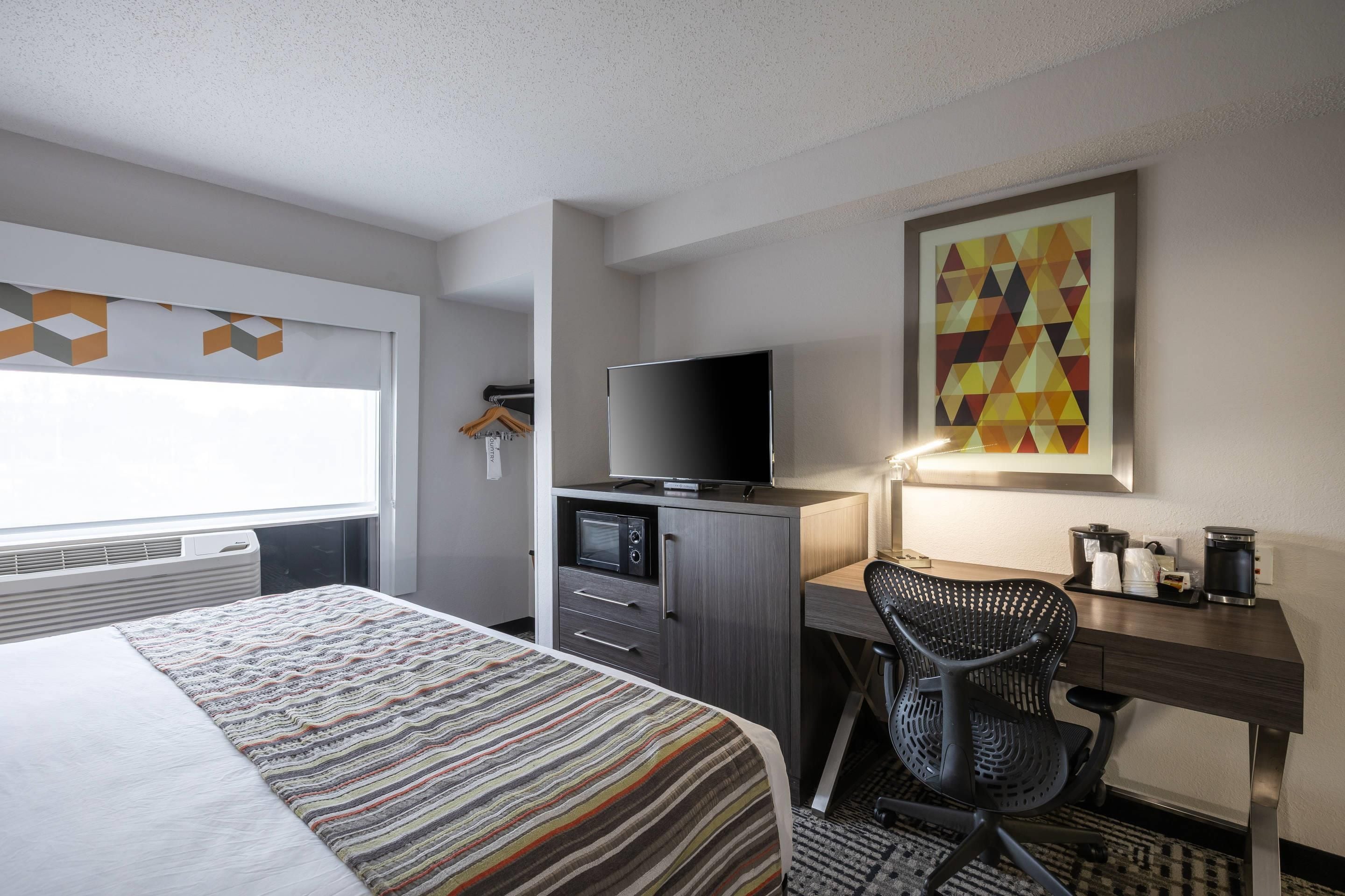 Una habitación de hotel con una cama, un escritorio con televisor, una silla y una cafetera.