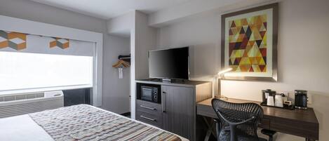 A hotel room with a bed, a desk with a television, a chair, and a coffee machine.