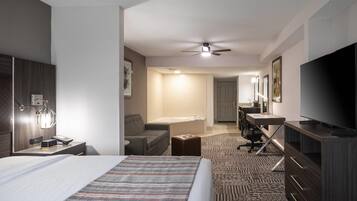 A hotel room with a bed, a desk, a chair, a television, and a ceiling fan.