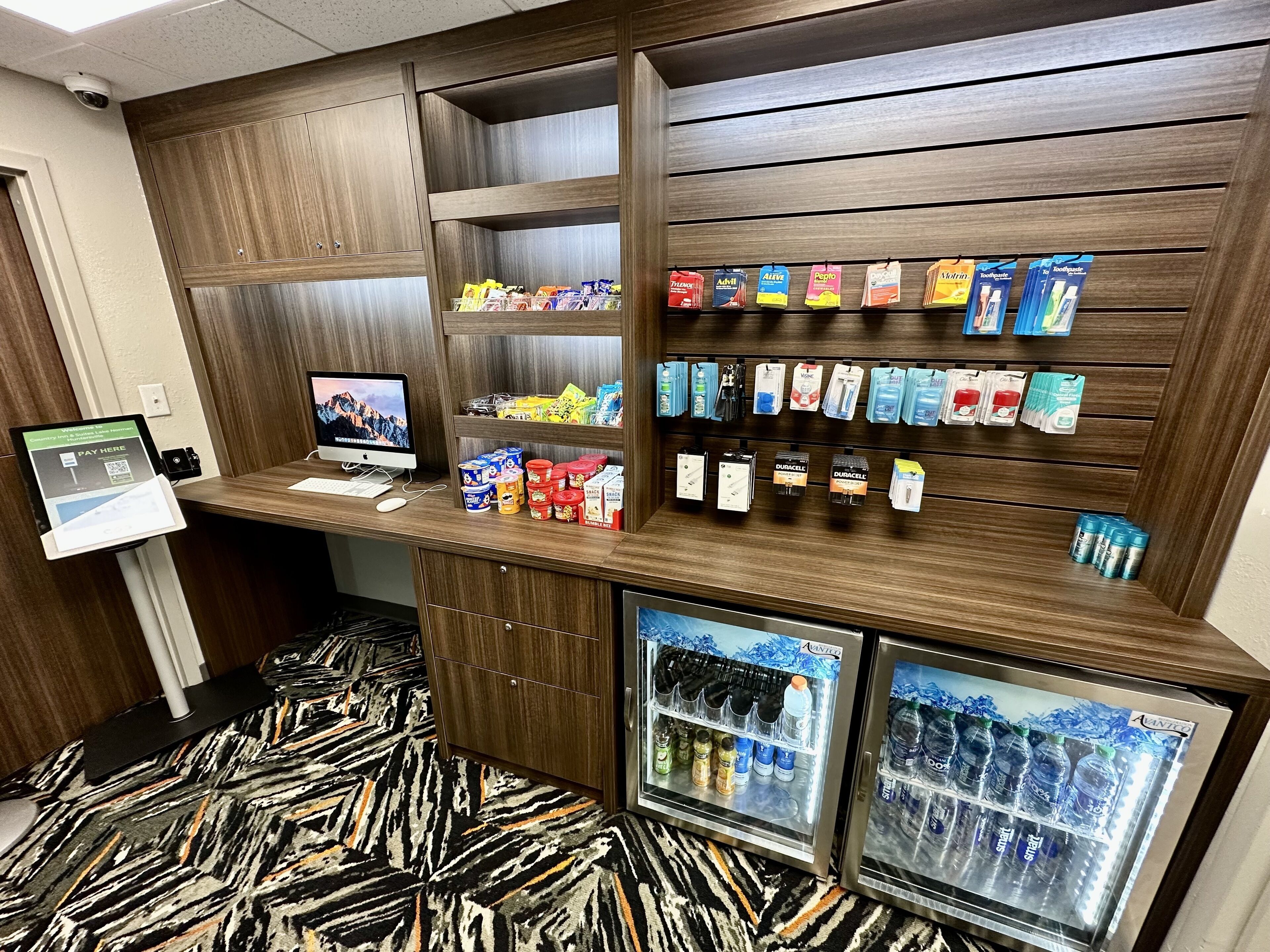 Un quiosco autoservicio con monitor de computadora, terminal de pago y una variedad de aperitivos y bebidas.