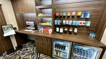Un quiosco autoservicio con monitor de computadora, terminal de pago y una variedad de aperitivos y bebidas.