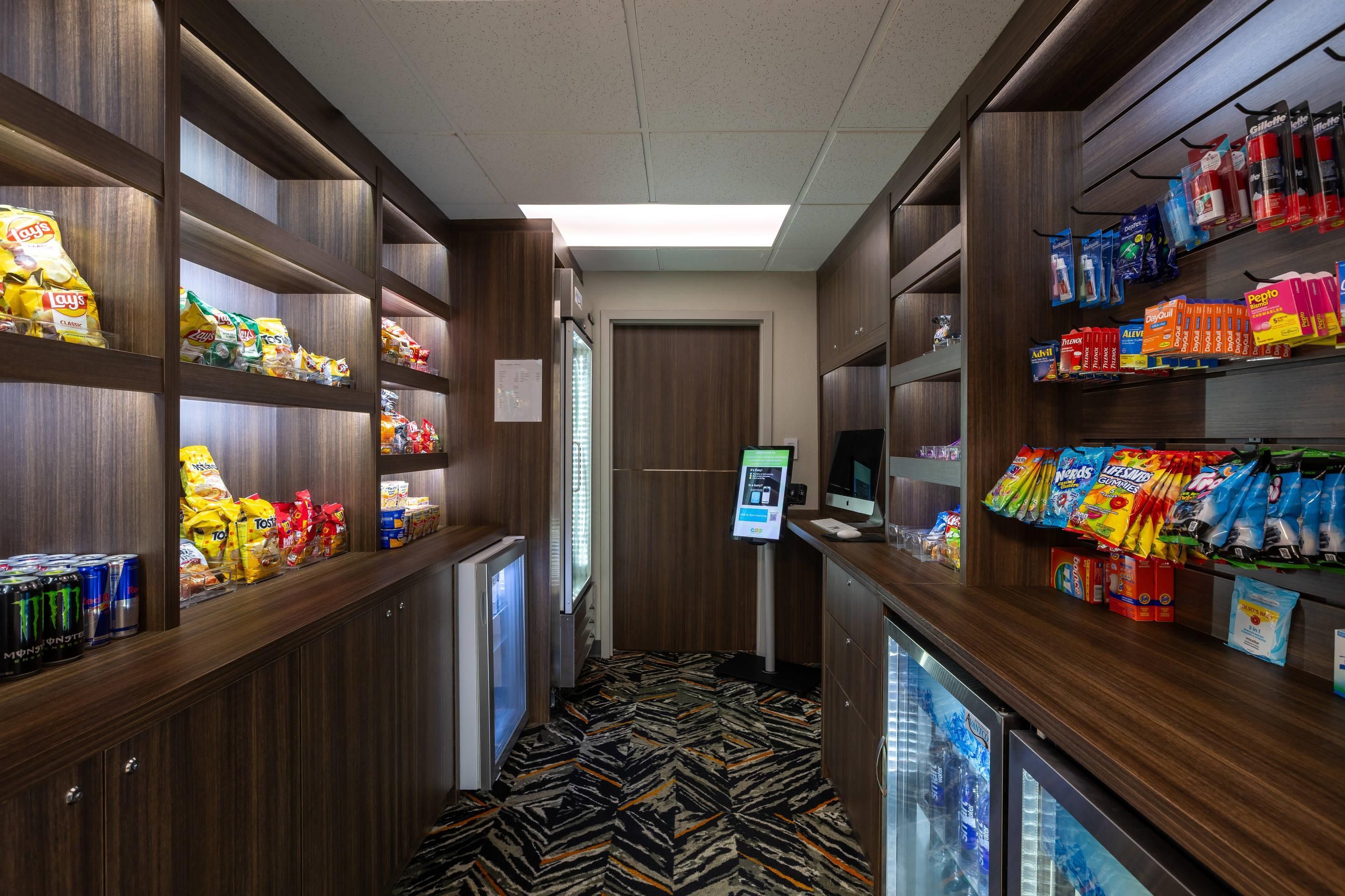 A hotel corridor with snack shelves, a refrigerator, and a digital kiosk.