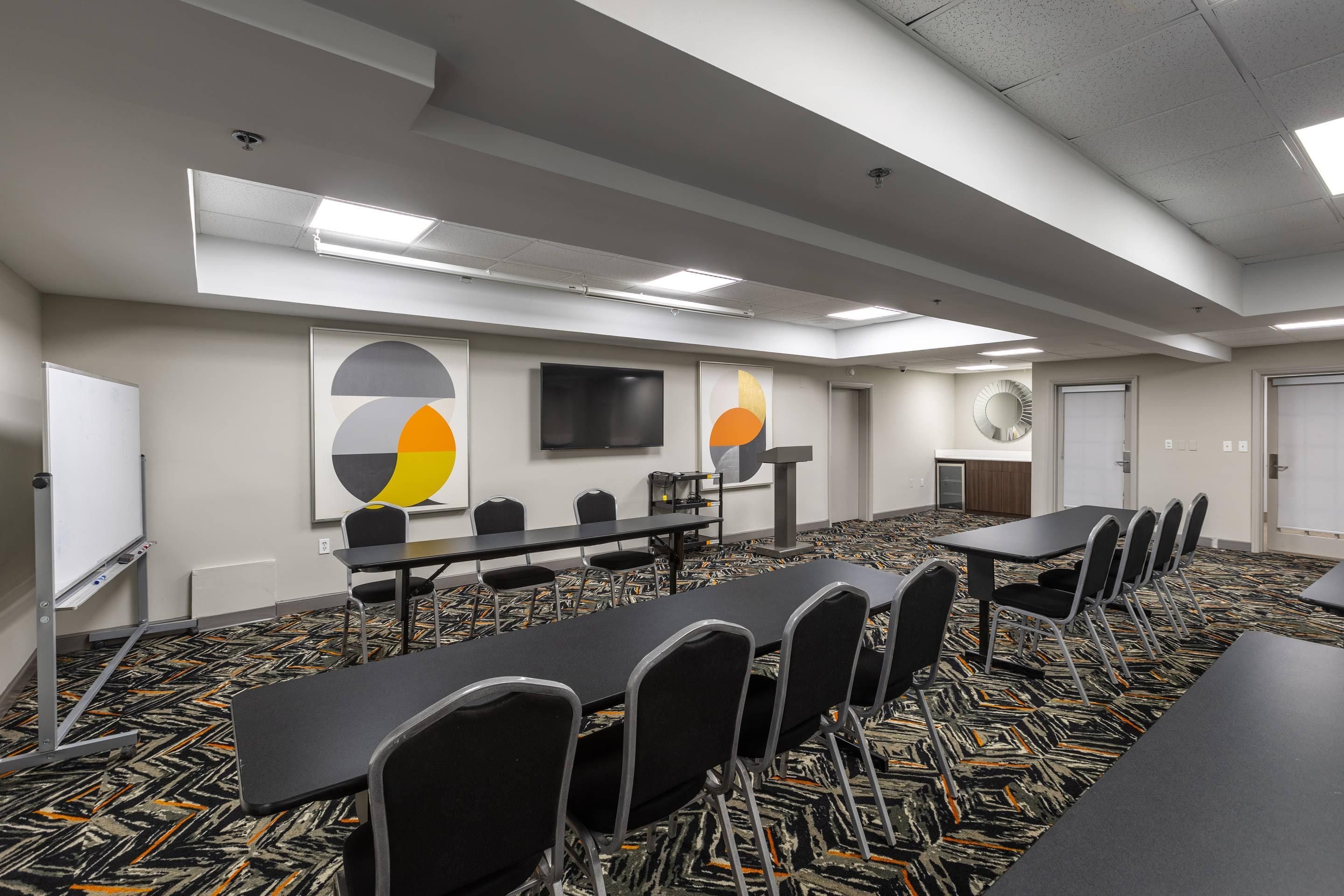 Uma sala de conferência com uma mesa comprida, cadeiras, um quadro branco e uma televisão.