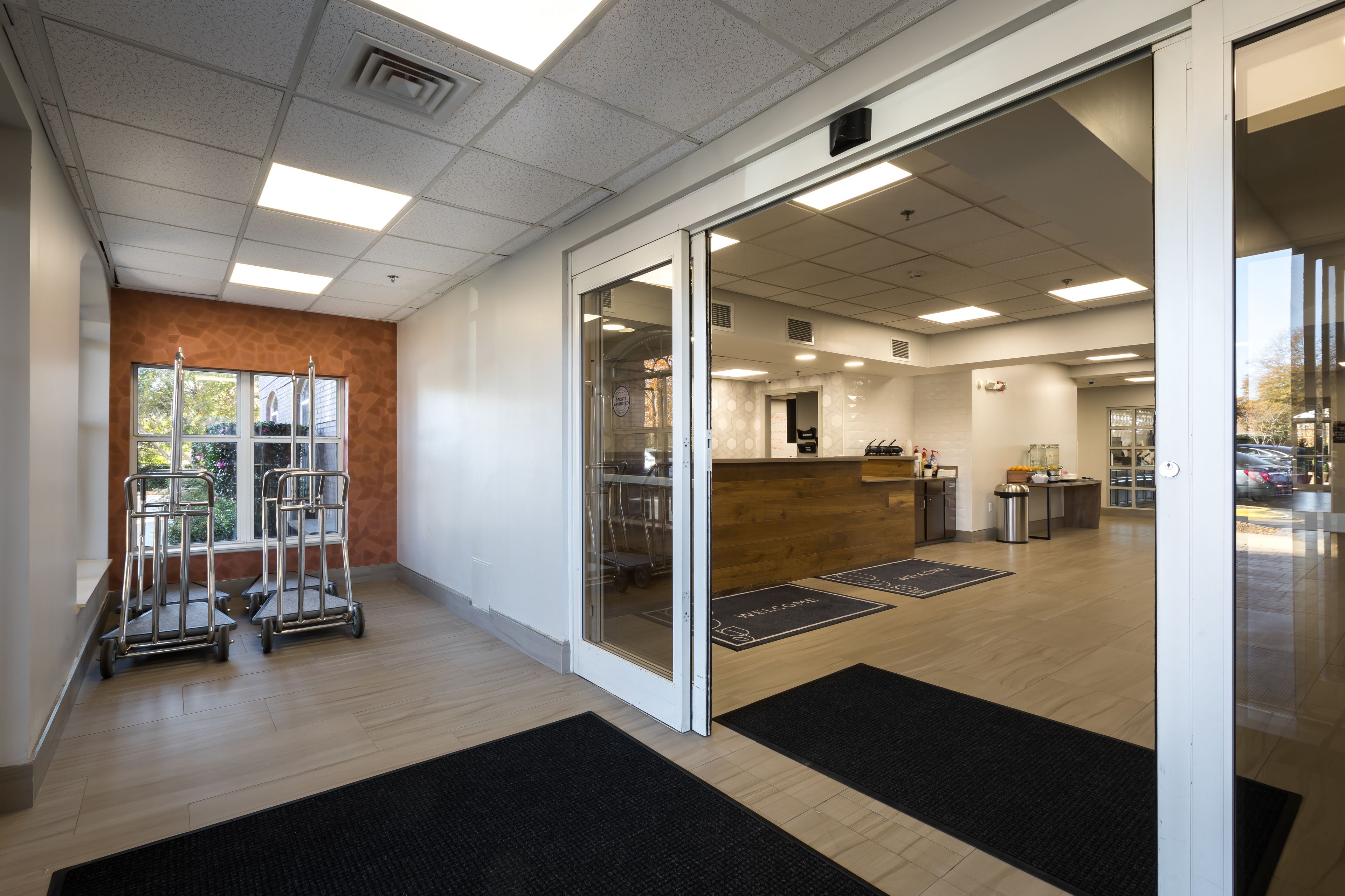 Eine moderne Hotellobby mit einer Rezeption, einer Kaffeestation und Blick auf den Parkplatz.