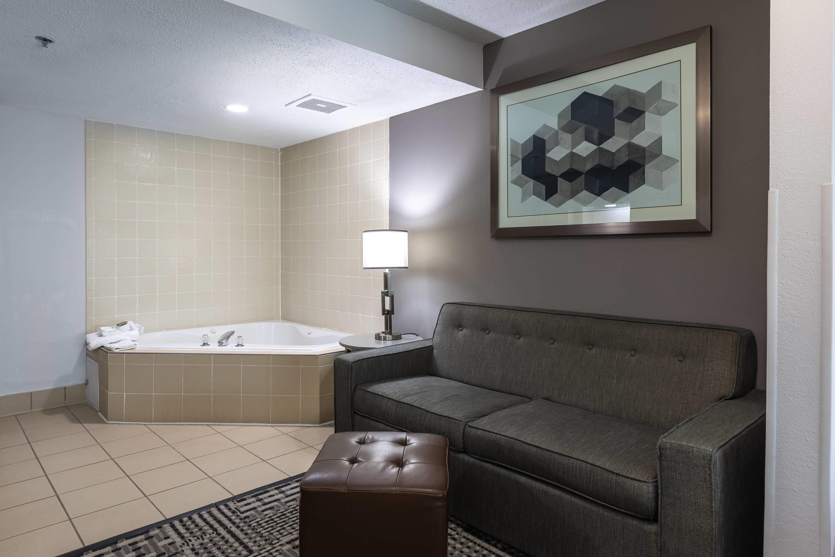 A modern bathroom with a bathtub, a grey sofa, and a framed geometric artwork on the wall.