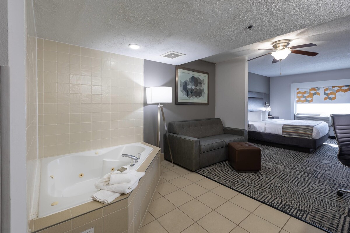 A modern bathroom with a bathtub, a gray sofa, a bed, and a ceiling fan.
