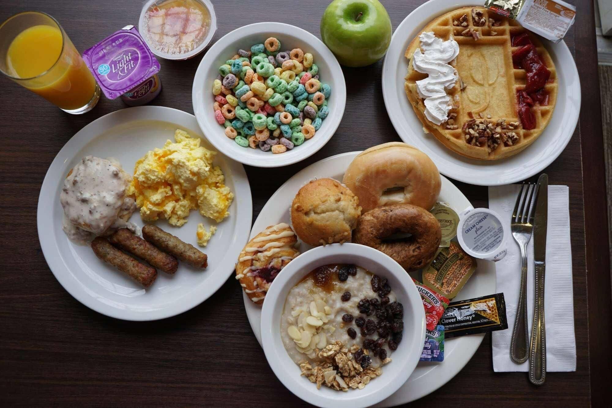 A breakfast spread with cereal, waffles, pastries, and a fruit.