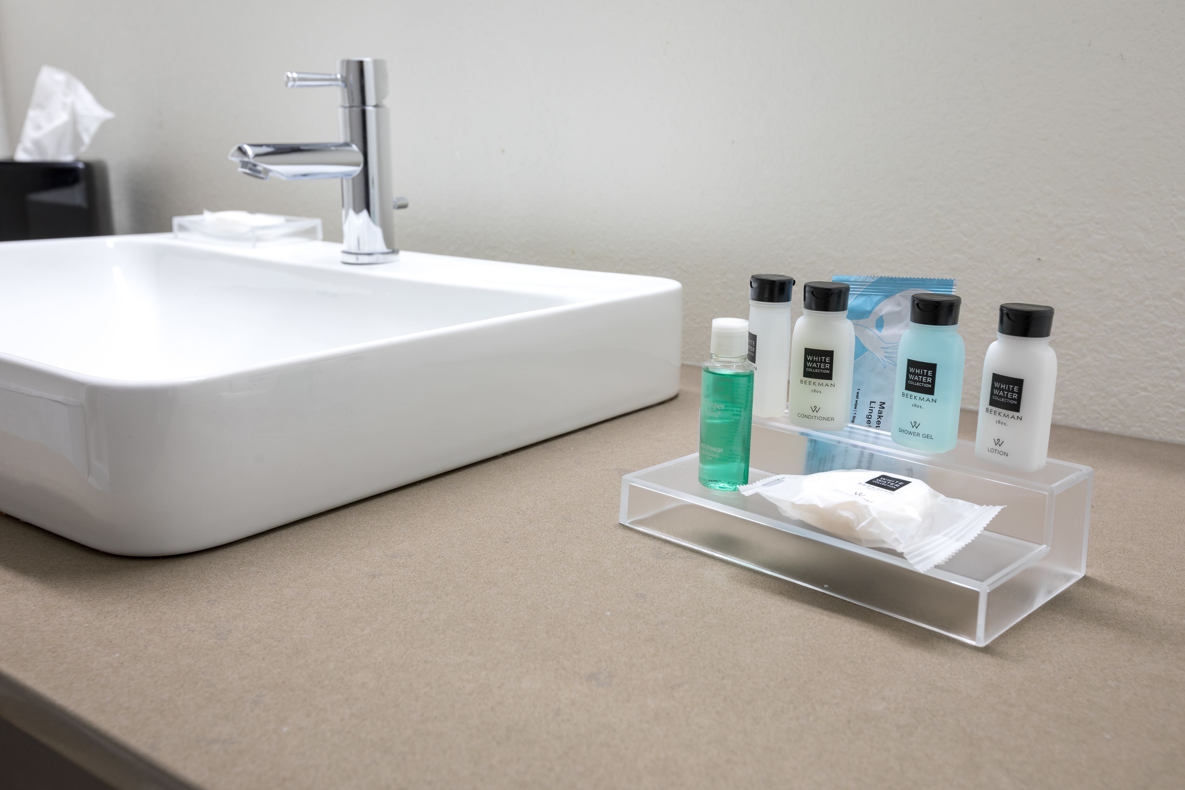 A bathroom sink with a clear soap dispenser and a set of toiletries on a transparent tray.