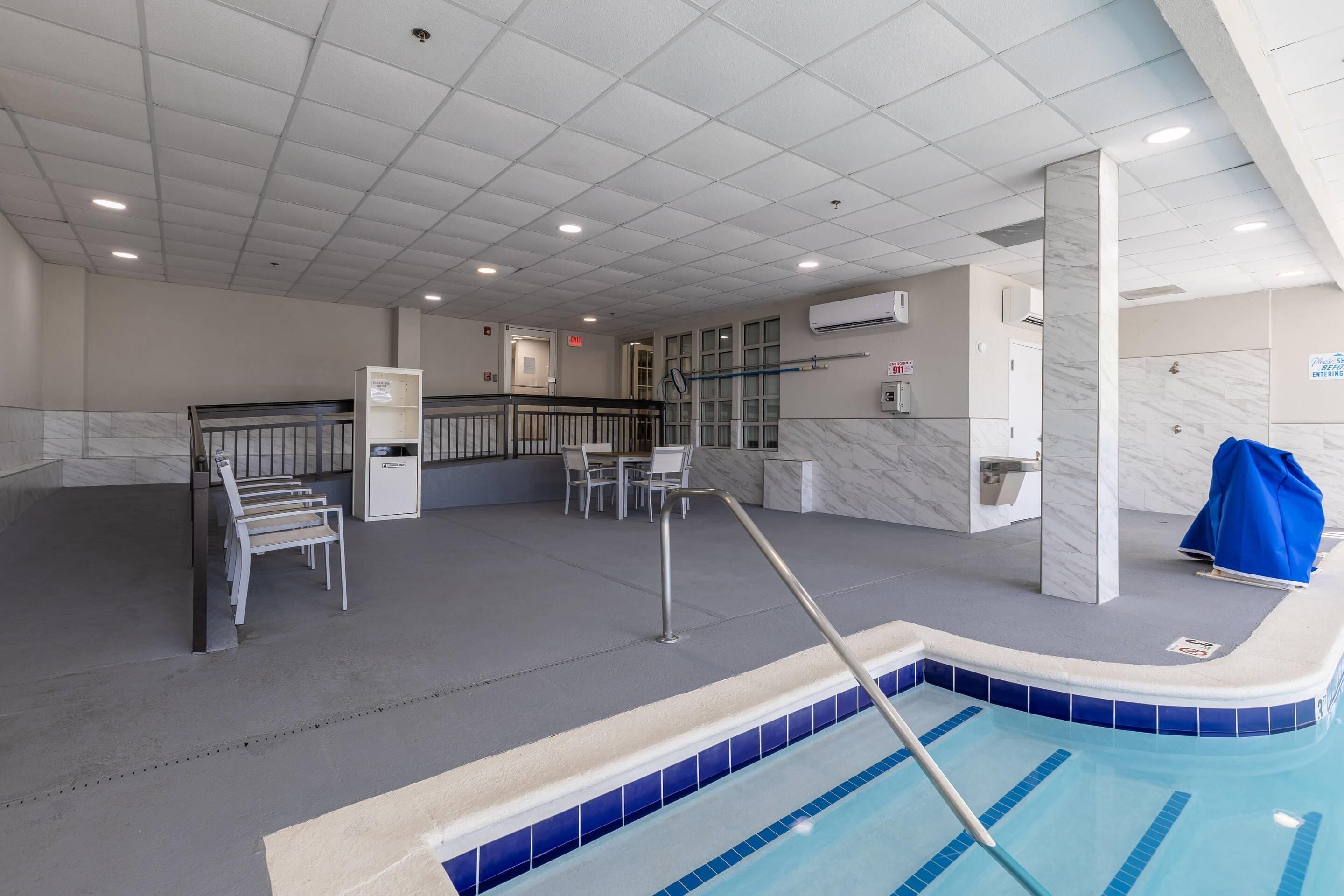 A swimming pool with a diving board, a changing room, and a seating area with chairs.