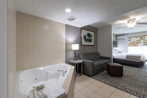 A modern hotel room with a large bathtub, a gray sofa, a small side table, and a bed with a patterned headboard. - Country Inn & Suites by Radisson, Lake Norman Huntersville, NC (Huntersville)