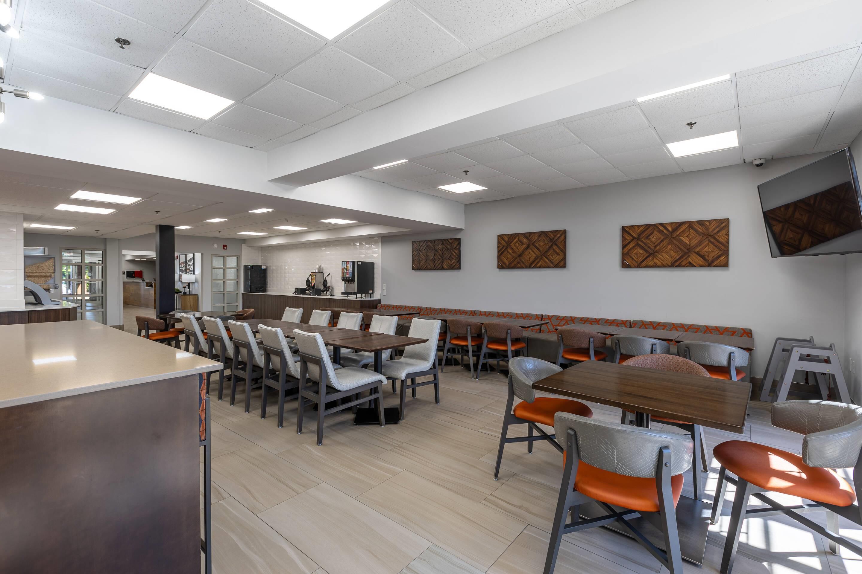 Una cafetería moderna con mesas y sillas altas, una barra larga y un televisor montado en la pared.