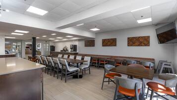 Una cafetería moderna con mesas y sillas altas, una barra larga y un televisor montado en la pared.