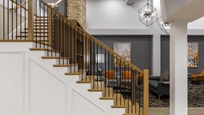 A staircase with wooden steps and black railings, leading to a living area with a gray sofa and orange cushions.