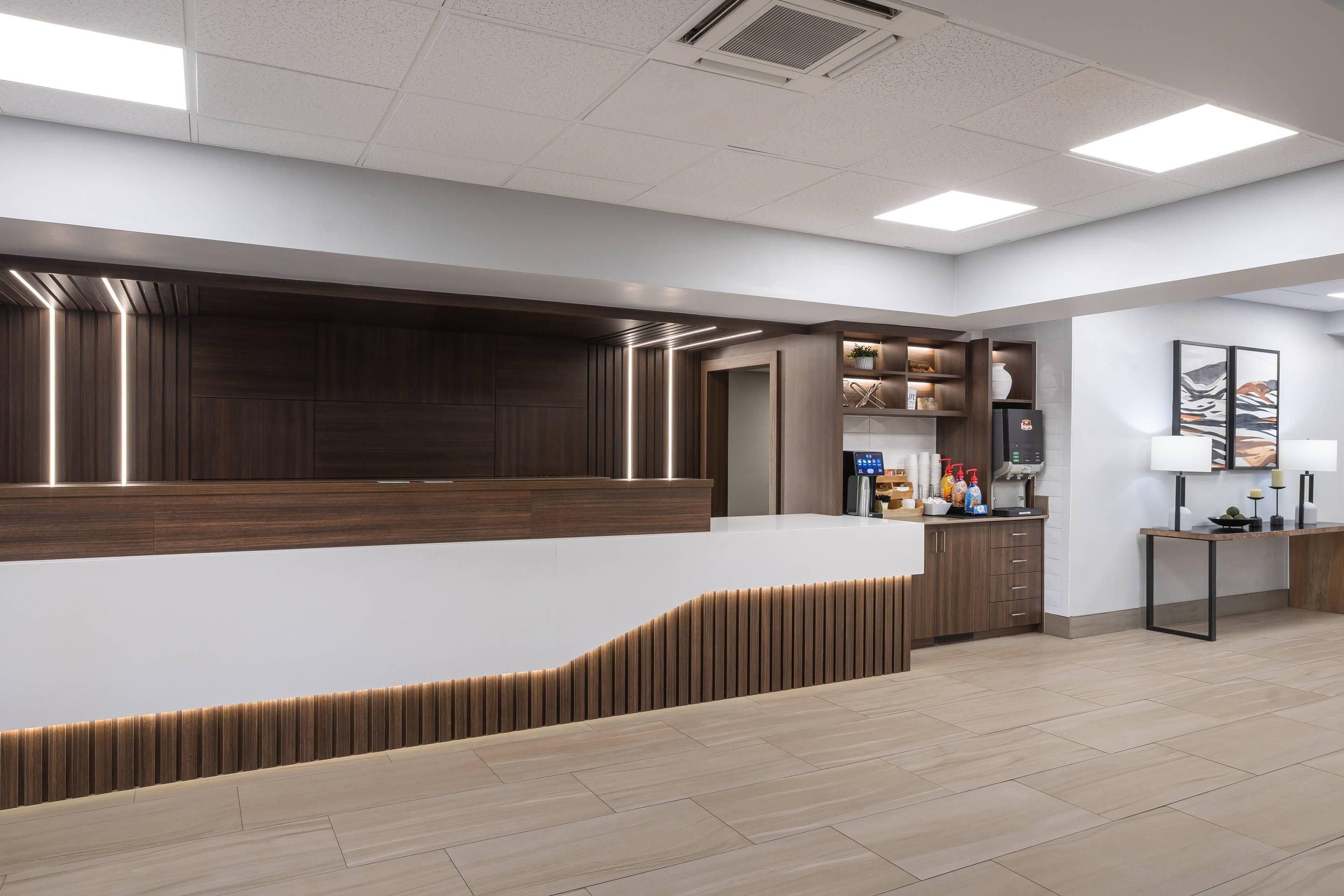 A reception area with a wooden reception desk, a small side table with a lamp, and a wall-mounted coffee machine.