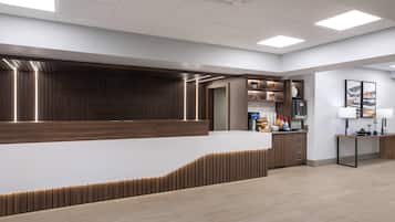 Zona de recepción con mostrador de madera, una mesita auxiliar con lámpara y una máquina de café instalada en la pared.