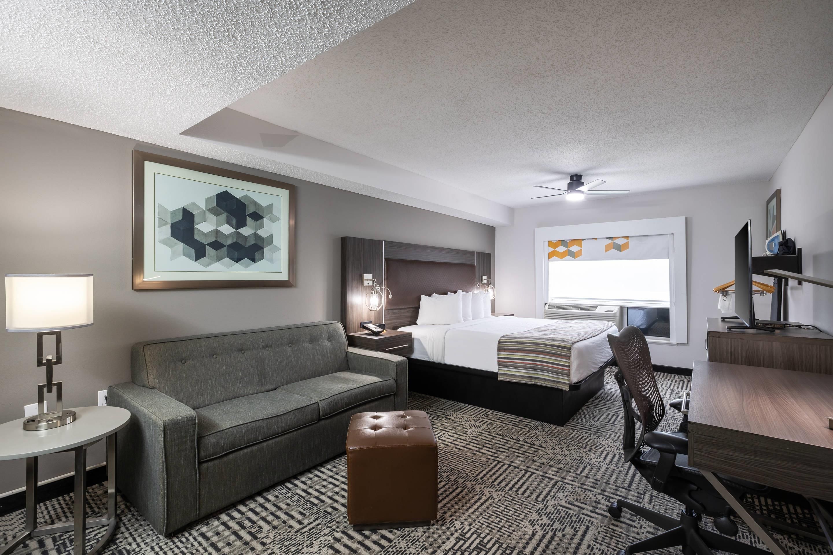 A hotel room with a bed, a sofa, a desk, a chair, and a small table.