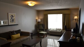 A hotel room with a sofa, armchair, and ottoman, a desk with a lamp, and a large window with curtains. - Country Inn & Suites by Radisson, Gurnee, IL (Gurnee)