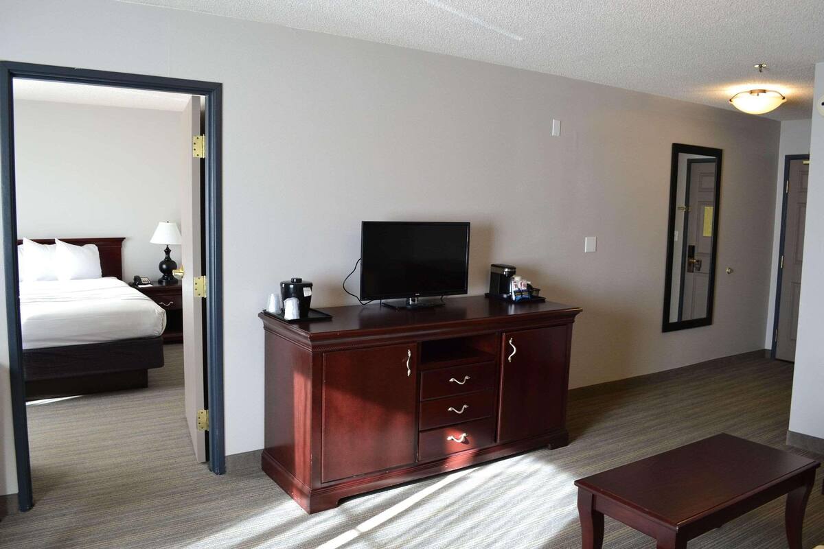 A hotel room with a wooden dresser, a flat-screen TV, a bed, and a small table.
