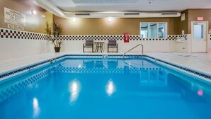 An indoor swimming pool with a checkered tile border, two chairs, a small table, and a potted plant. - Country Inn & Suites by Radisson, Gurnee, IL (Gurnee)