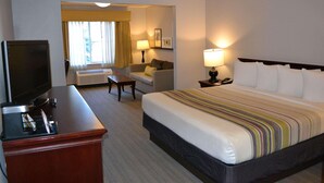A hotel room with a bed, a desk with a television, a sofa, and a lamp. - Country Inn & Suites by Radisson, Gurnee, IL (Gurnee)