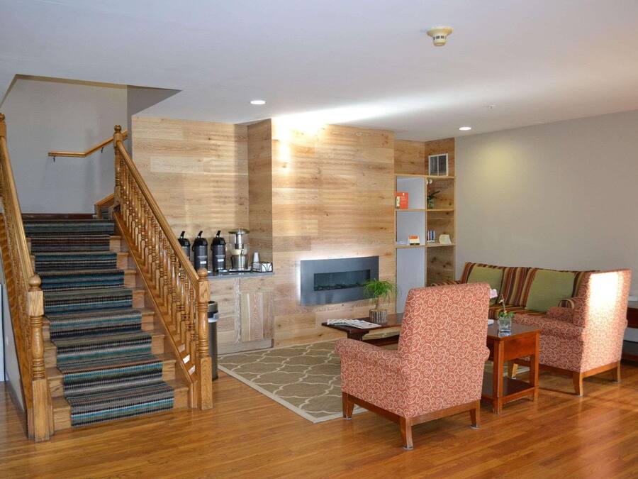A spacious living area with a wooden staircase, a fireplace, and a seating area with patterned chairs.